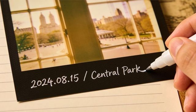 Writing date on black-border instant print with white marker for scrapbook journaling