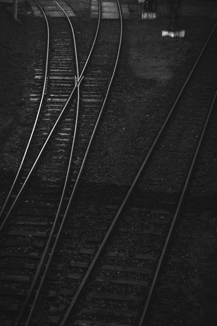 Dimly lit scene of converging railroad tracks in black and white. Appropriate for themes related to transportation, industrial settings, connectivity, travel, and historical imagery. Suitable for articles, backgrounds, or artistic projects emphasizing moody, timeless elements.