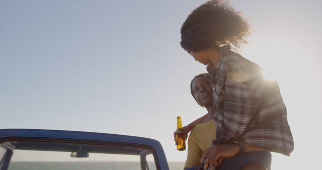 Couple relaxing at beach during sunset holding beers. Ideal for advertisements in hospitality, vacation and relaxation, romantic getaways, and evening moments.