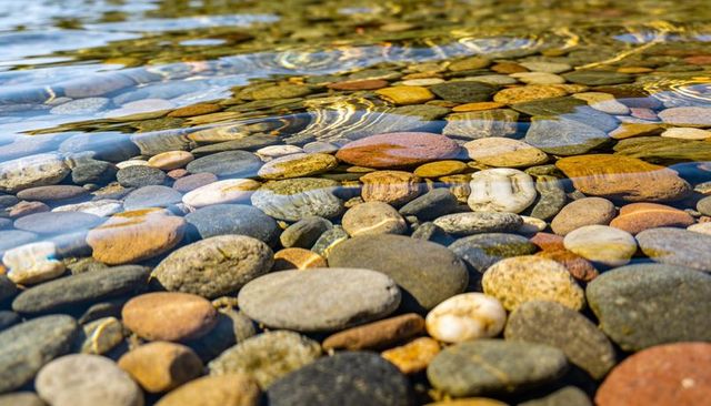 Glittering river pebbles under clear water with colorful caustic ripples and texture
