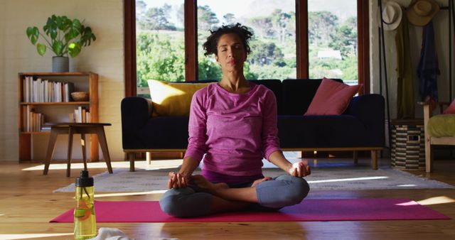 Biracial woman practicing yoga and meditating while sitting on yoga mat at home. staying at home in self isolation in quarantine lockdown