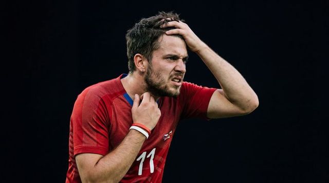Grimacing male athlete clutching head pulling red jersey 11 showing intense focus