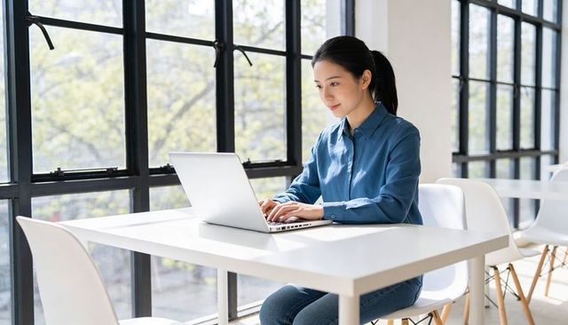 Young woman working on laptop in bright modern workspace by window