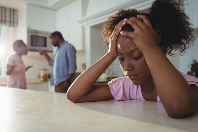 This image depicts a young girl looking sad and distressed while her parents argue in the background in a kitchen. It can be used in articles or campaigns related to family conflict, child psychology, domestic issues, and the impact of parental arguments on children. It is also suitable for illustrating topics on emotional well-being and family dynamics.