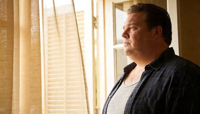 Mature man gazing through sunlit window, contemplating in warm diffused light