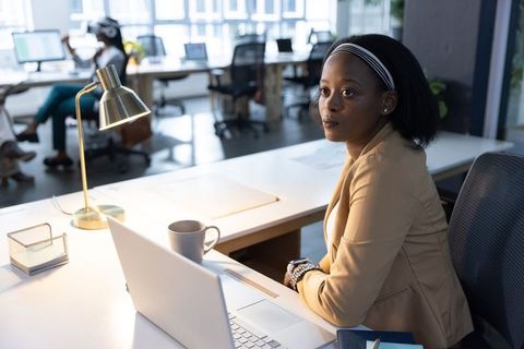 Professional woman in tan blazer working at laptop in modern open-plan office