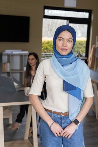 Confident muslim professional wearing blue hijab and smartwatch in modern coworking space with team