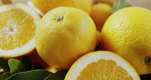 Bright yellow lemons, some cut to reveal the juicy interior, are grouped together, showcasing their fresh and vibrant appearance. Lemons like these are often used in culinary dishes and beverages for their tangy flavor and aroma.