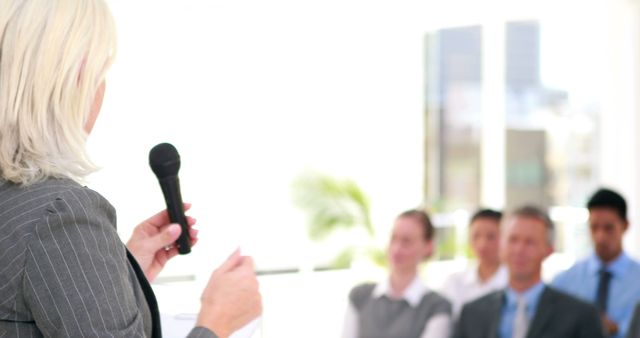 Businesswoman giving a presentation to colleagues in an office setting. Suitable for use in materials related to corporate training, seminars, team meetings, professional development, and workplace communication.