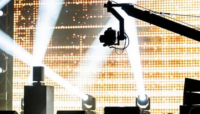Camera crane silhouette stretching across concert stage against led wall and moving lights