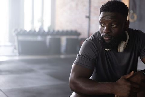 African american man resting on gym bench wearing headphones showing recovery and focus