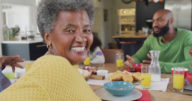 Image of happy african american grandmother turning and smiling at family breakfast table. Family, domestic life and togetherness concept digitally generated image.