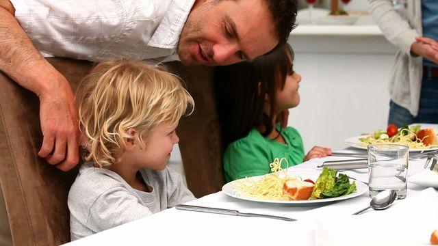 Young children seated at dinner table with attempted encouragement from father to try vegetables. Focus is on balanced diet, showing educational moment in parenting. Ideal for family lifestyle illustrations, nutritional advice articles, or educational content about healthy eating habits.