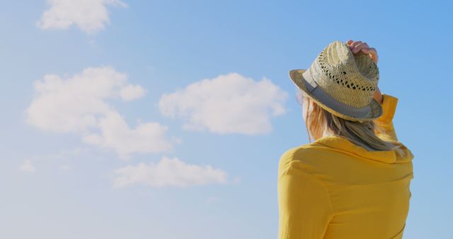 A woman in a yellow top and straw hat looks out towards the sky, with copy space - Download Free Stock Photos Pikwizard.com