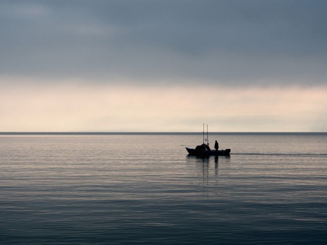 Fishermen on a boat during dawn over a calm lake creating a peaceful serene moment ideal for themes of tranquility, solitude, nature, and fishing. Perfect for use in travel content, promoting outdoor activities, mental well-being, relaxation, and leisure sports.
