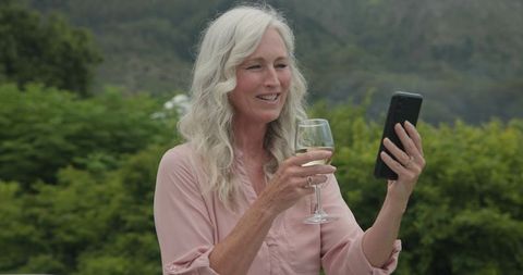 Smiling Woman with Wine Glass Video Calling Outdoors in Scenic Setting