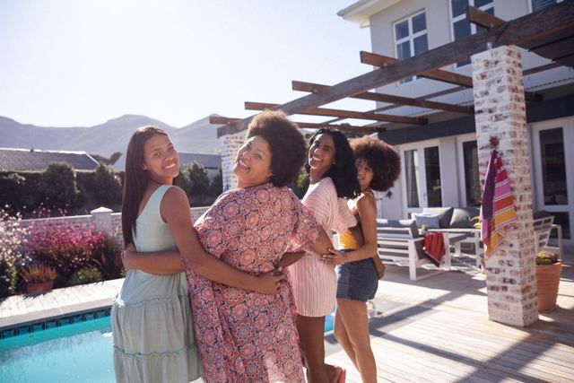 Group of happy biracial female friends standing by the poolside, smiling and enjoying a summer day together. Perfect for concepts related to friendship, social gatherings, leisure activities, and summer vacations. Ideal for use in lifestyle blogs, travel websites, and advertisements promoting outdoor fun and relaxation.