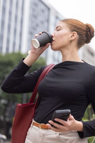 African american professional sipping coffee while checking phone on urban commute
