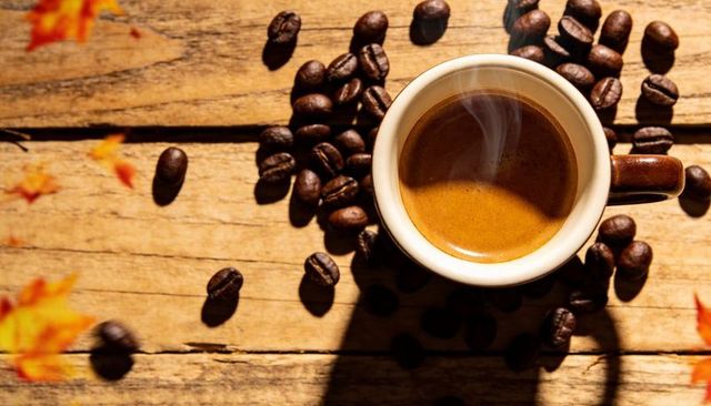 Steaming espresso cup sitting on rustic wood with scattered coffee beans and autumn leaves