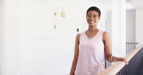 Smiling african woman standing on landing leaning on wooden railing wearing pink top