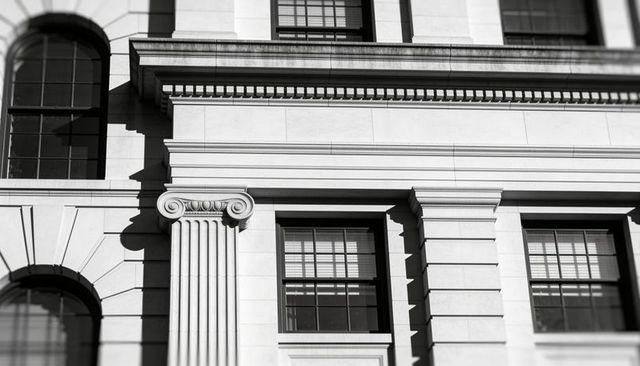 Neoclassical stone facade with ionic column and strong shadow contrast in monochrome