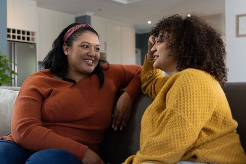 Two friends chatting on sofa in cozy modern living room wearing knit sweaters