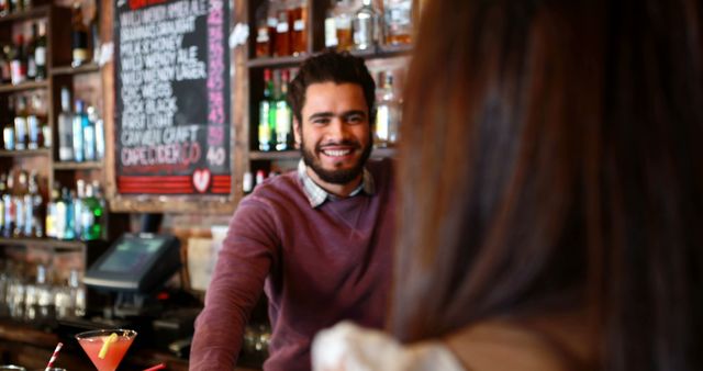 Bartender in casual clothes smiling while interacting with a customer, suggesting enjoying a night out. Ideal for uses in hospitality marketing, nightlife promotions, customer service training, and advertisements for bars and restaurants.