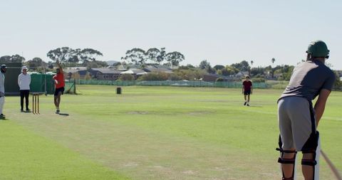 Cricket batsman facing bowler on lush pitch with umpire and fielders, match action