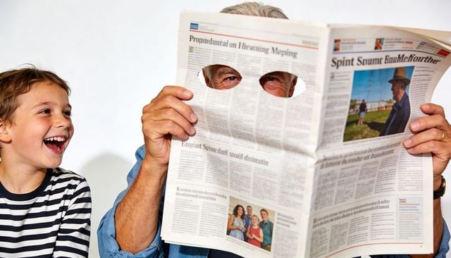 Grandfather peeking through newspaper eyeholes while grandson laughing in family moment