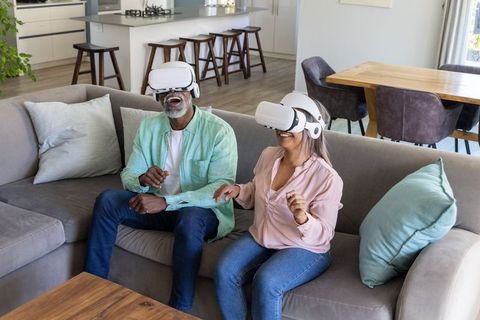 Older couple enjoying virtual reality headsets at home on modern living room sofa