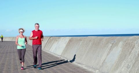 Active senior couple jogging along coastal pathway