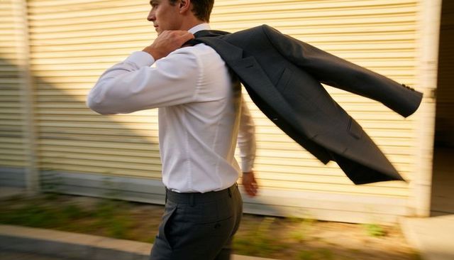 Businessman walking with jacket over shoulder at golden hour urban corridor motion blur
