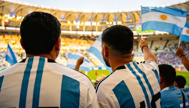 Argentina fans cheering and waving flags in energetic stadium crowd under evening lights