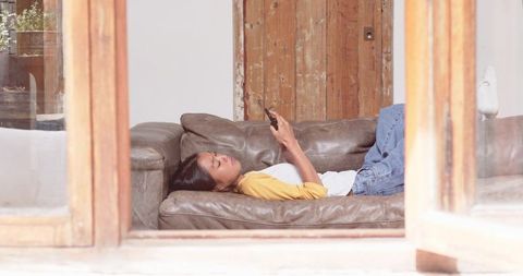 Relaxed Woman Lounging on Sofa with Smartphone in Modern Living Space