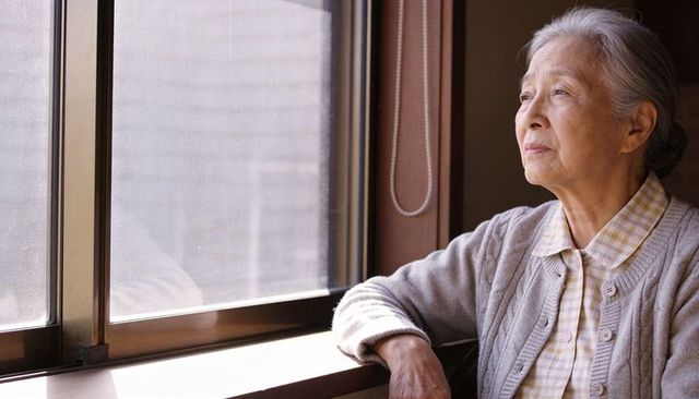 Senior asian woman gazing out window in cardigan, contemplative elder at home