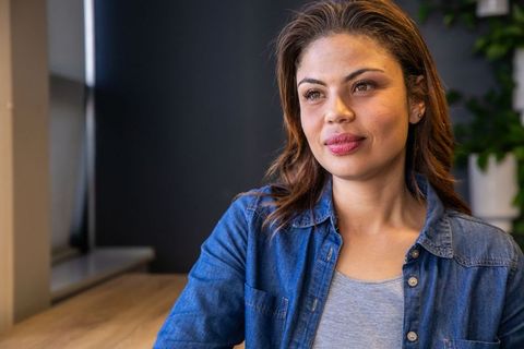 Thoughtful woman sitting at wooden table by window in minimalist workspace lounge