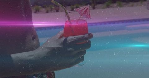 Shirtless man holding pink cocktail poolside wearing floral swim trunks summer relaxation