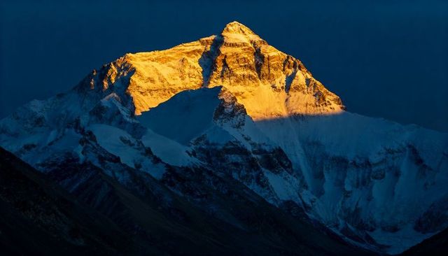 High-altitude snow-covered mountain summit bathing in golden alpenglow at sunrise with glacier shado