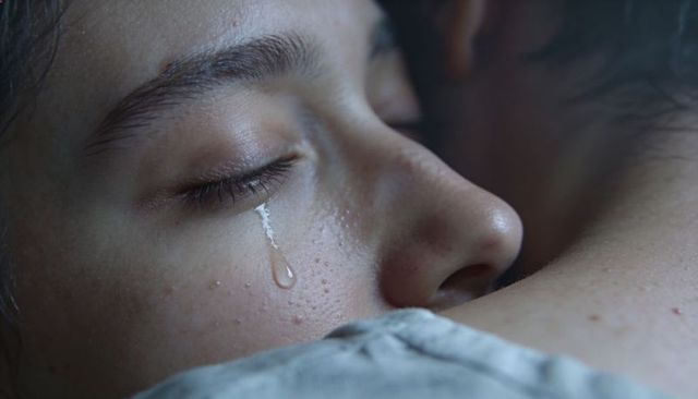 Close-up of woman crying while embracing partner, single tear on cheek conveying emotion
