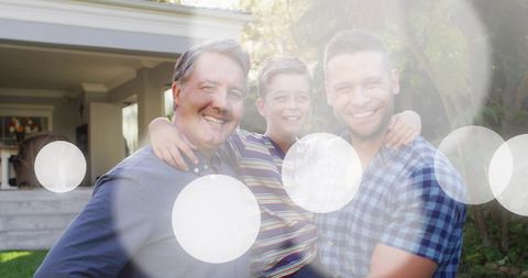 Smiling grandfather father and son embracing in sunny front yard with lens flare