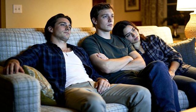 Three young adults relaxing on couch together in cozy living room with warm lamp light