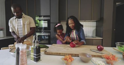 African American family preparing healthy dinner together at modern kitchen island