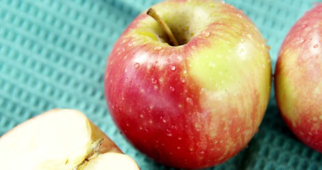 Close-up of fresh red apples with water droplets on blue towel. Perfect for use in advertisements for healthy snacks, organic produce promotions, or grocery store displays. Captures freshness and natural appeal of fruit.