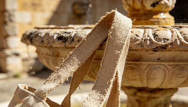Frayed burlap tote straps draping over carved stone fountain rim rustic texture close-up