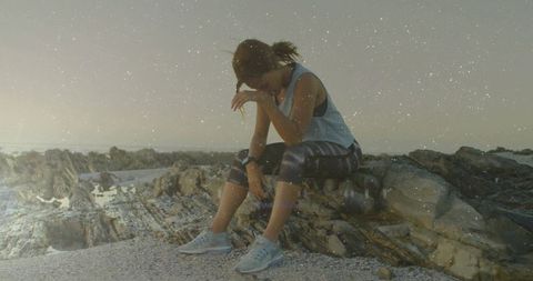 Exhausted female athlete resting on rocky beach in early morning light