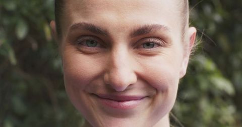 Close-up smiling woman showing natural skin texture and freckles, calm outdoor headshot
