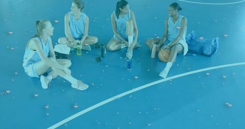 Women basketball players sitting on blue court taking break with water bottles and pink confetti
