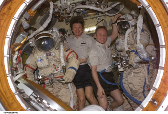 Astronauts are in the Pirs Docking Compartment on the International Space Station, posing with their Russian Orlan spacesuits. This scene highlights teamwork, the working conditions in space, and human efforts in space exploration. Perfect for articles about space missions, travel, technology advancement in space, and multinational collaboration in space exploration.