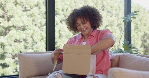 Smiling woman unboxing cardboard package in bright living room
