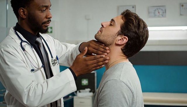 Physician palpating patient neck during clinical throat exam in modern medical clinic